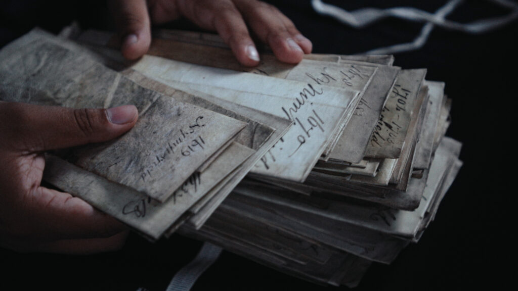 A close up of a person sorting through a pile of 17th century handwritten documents.